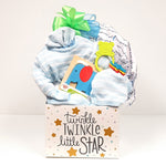 A cute baby gift box holding a knit outfit or sleeper, a receiving blanket, baby bib, teething rattle and classic baby puzzle for the new little star.