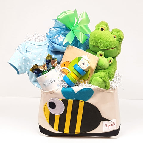 A tote gift basket brimming with a onesie, receiving blanket, plush toy, classic baby rattle, puzzle and for mom a keepsake mug with a few delectable truffles