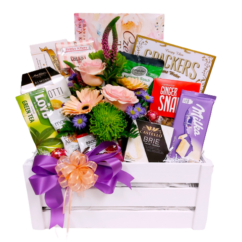 Our pretty white crate gift basket comes filled with a beautiful floral arrangement and a wonderful assortment of sweet & salty treats, cheese & crackers and some to tea to enjoy. So much to savour!