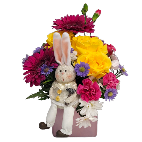 Designed in a pretty pink glass cube vase is a fresh assortment of bright blooms with a cute keepsake bunny nestled inside.  