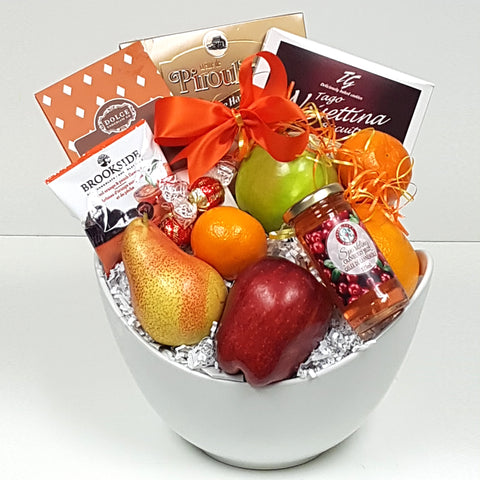 Cookies, specialty chocolates and some sparkling jelly too nicely arranged with some fruit in a beautiful ceramic fruit gift basket bowl.