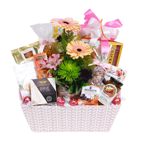 Pretty basket filled with chocolates, crackers and cheese, jam, sweet treats and a pretty floral arrangement nestled inside.