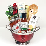 A classy red gourmet gift basket colander brimming with pastas, Italian pasta sauce, crackers, savoury shortbread, gourmet dipping sauce and a wooden pasta spoon.