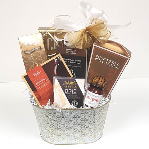 A beautiful white and gold tin gift basket filled with crackers and cheese, maple glazes smoked salmon, pretzels, red pepper jelly, cookies & chocolate too.