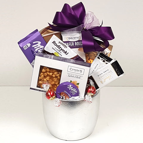 A silver ceramic pot gift basket nestled with Lindt chocolate, chocolate covered raisins, a salty snack mix, chocolate treats, wafer rolls and pretzels too!