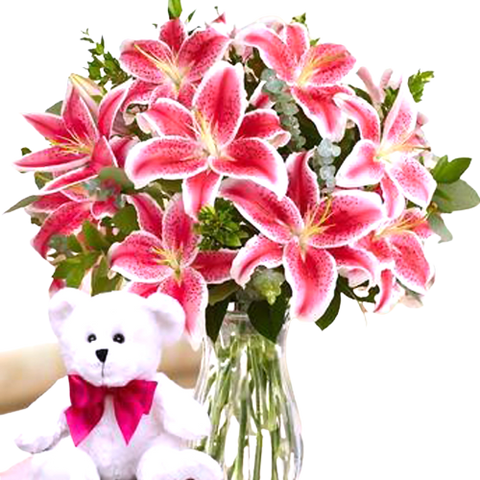 Full vase arrangement of lilies with a plush bear to beautifully adorn the gift.